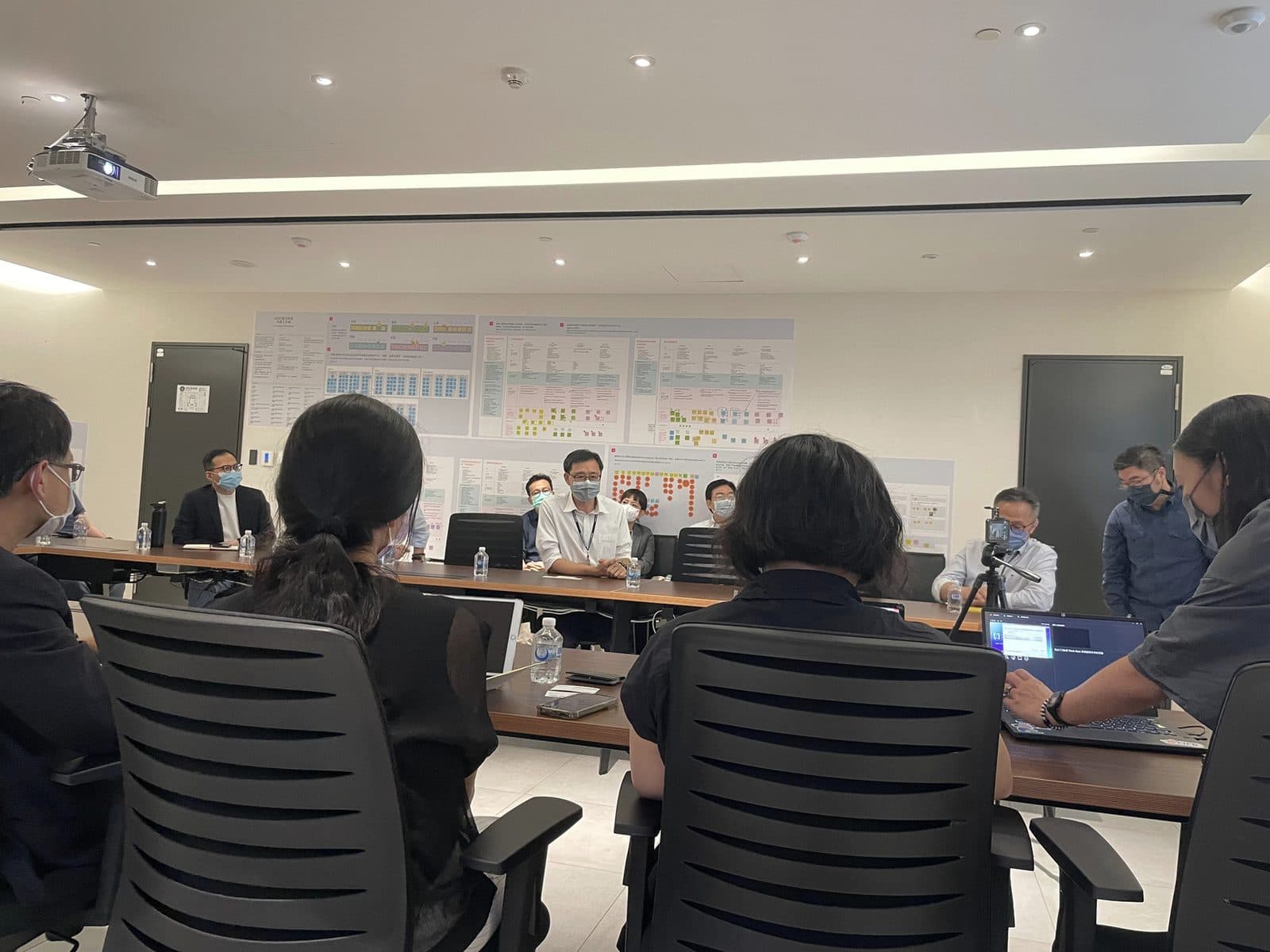 Briefing ASUS leadership in a meeting room, with the synthesized research wall — journey maps and clustered HMW votes — behind the table